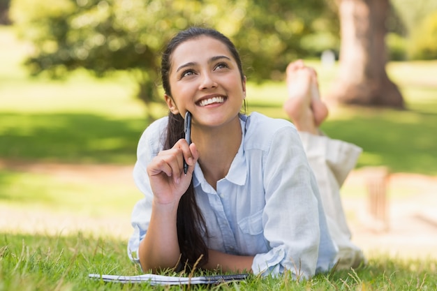 Thoughtful woman with book and pen relaxing in park