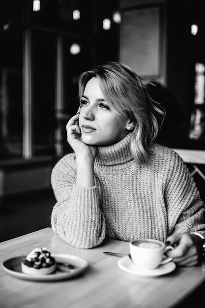 Photo thoughtful woman with coffee and pastry woman sits at table holding coffee cup with one hand look