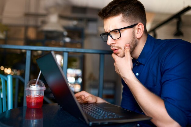 Thoughtful young attractive hipster freelancer working remotely on laptop in loft cafe businessman