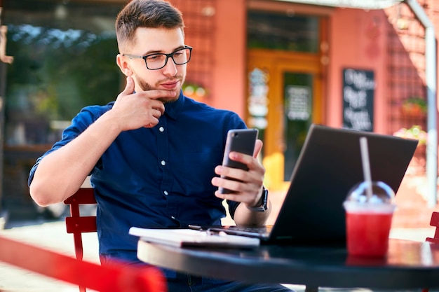 Thoughtful young businessman holding modern smartphone freelancer with a mobile phone thinks about