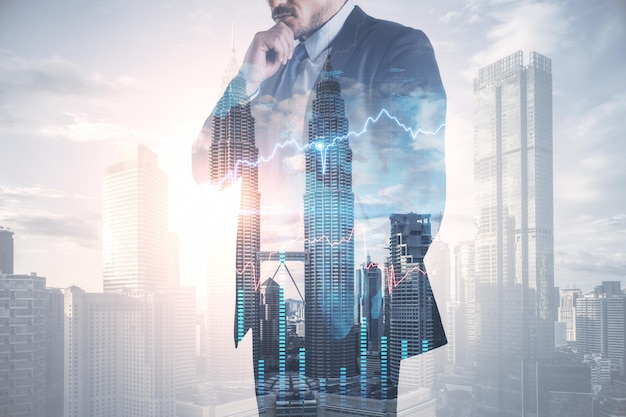 Thoughtful young european businessman in suit standing on abstract bright city background with forex chart and mockup place Finance trade and success concept Double exposure