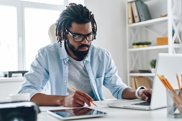 Thoughtful young man in eyewear using computer while working indoors