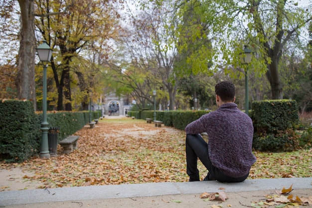 Thoughtful young man sitting on stairs in autumn park and looking away.