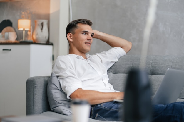 Thoughtful young man with a laptop sitting on couch