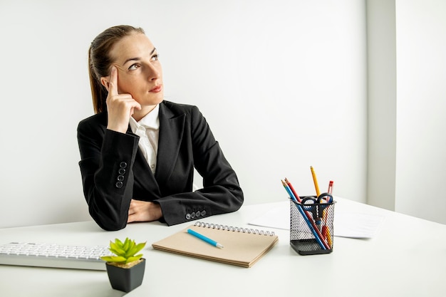 Thoughtful young woman in jacket sitting at table at workplace