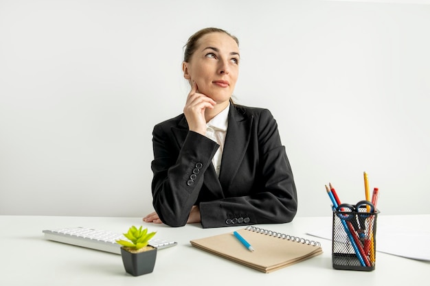 Thoughtful young woman in jacket sitting at table at workplace