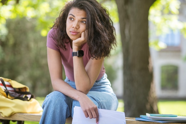 In thoughts. Long-haired pretty mulatta sitting on the bench with a thoughtful look