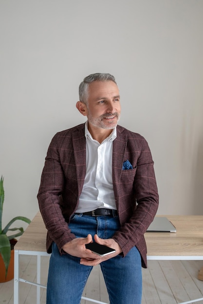 In thoughts. A man in brown jacket standing near the table and looking thoughtful