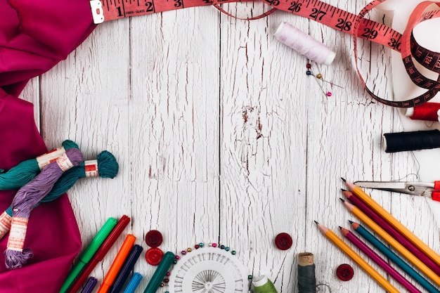 Photo threads, needles, pencils, cloth, tape measure make a circle on white wooden table