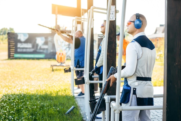 Three adult mans in sunglasses protective headphones and a rifle vest practicing fire weapon shoot