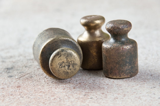 Three antique bronze weights for scales on concrete.