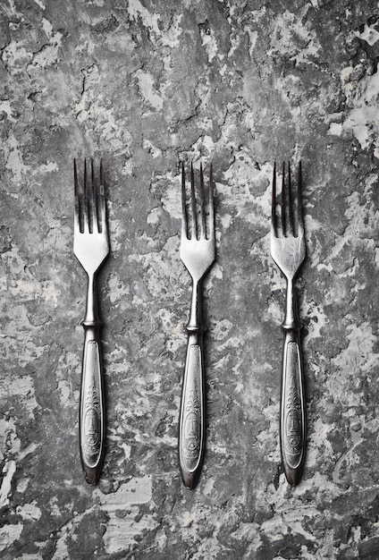 Three antique forks on a gray concrete table. Top view.