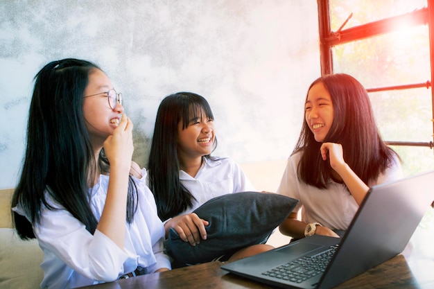 Three asian teenager laughing with happiness face while working on aptop in living room