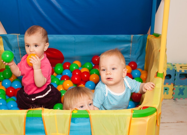 Three babies playing with multicolored small balls inside the playpen