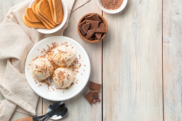 Three balls of ice cream with chocolate chips and cookie crumbs in a white plate on a light wall