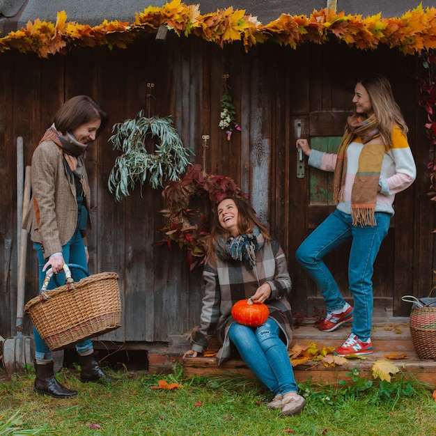 Photo three beautiful young women, having fun with a yellow autumn leaf, smiling on an old wooden background. the autumn fashion season.