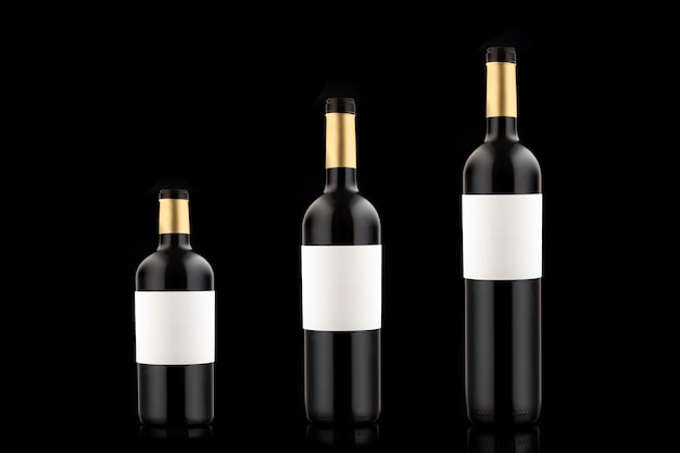 Three bottles of red wine with empty labels of different volume and size on a black background