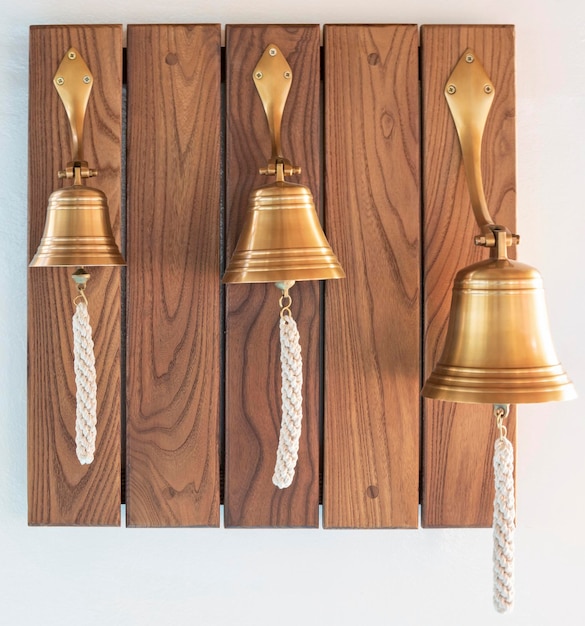 Three brass ship39s bells with ropes hanging on wooden wall