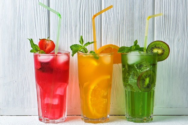 Three bright colored delicious cold lemonade carafes of kiwi and orange and strawberry with mint against the surface of a wooden white wall