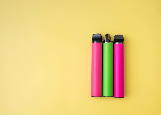 Three bright electronic cigarettes lie on a yellow background place under the inscription