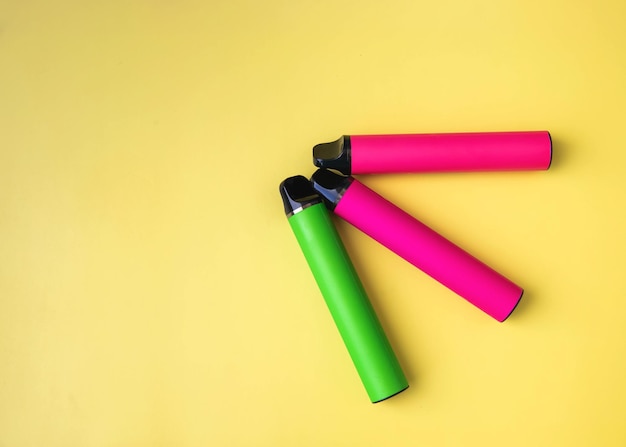 Three bright electronic cigarettes lie on a yellow background place under the inscription