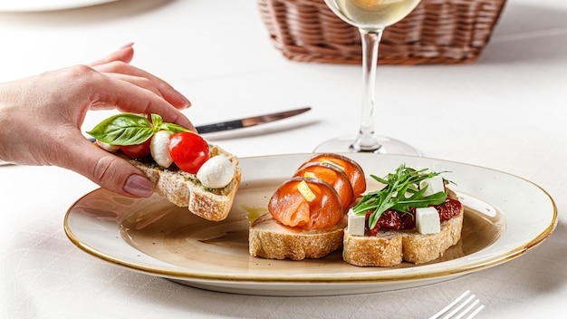 Three bruschettas on a white plate with cheese, cherry tomatoes, basil, loss, sun-dried tomatoes