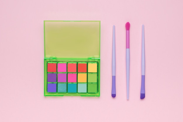 Three brushes and a set of multicolored eyeshadow on a light pink background Flat lay