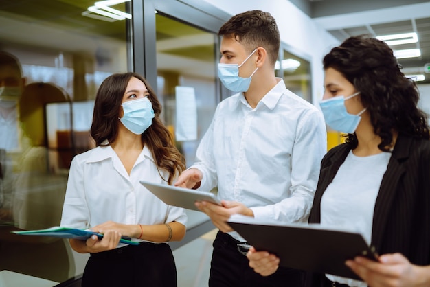 Three business colleagues in protective face mask discussing work related matters on an office.