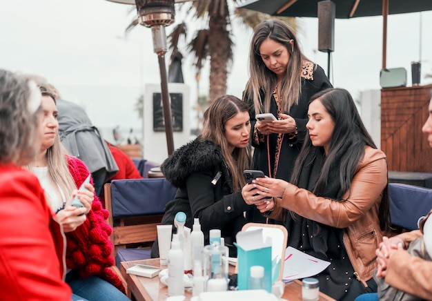 Three business women looking at cellphone in sale of dermatological products with customers at outdoor table