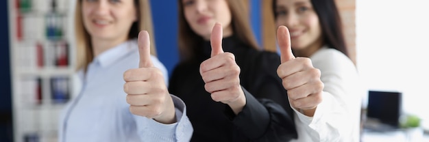 Three businesswoman smiling and holding thumbs up in office