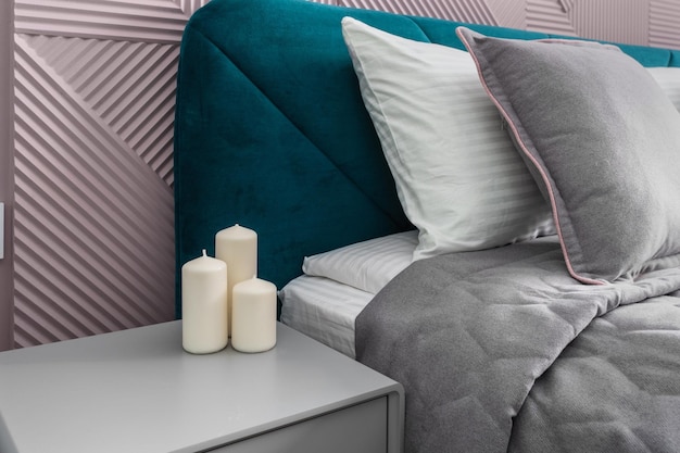 Three candles on the bedside table against the background of the bed and two pillows