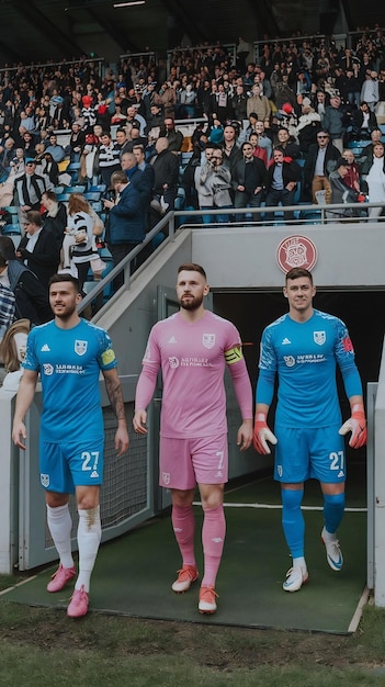 Three Caucasian Footballers Walking Out of the Tunnel onto the Sports Stadium Field