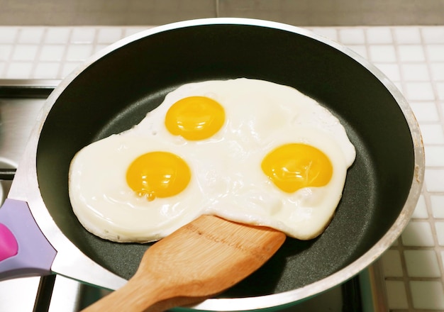 Photo three of chicken eggs sunny side up being fried in a pan