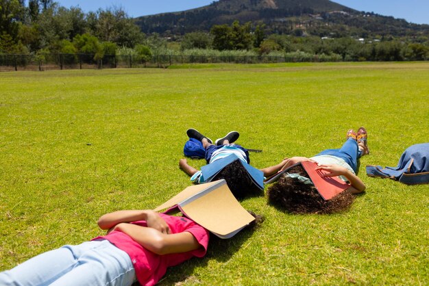 Photo three children are lying on the grass with books beside them facing away from the camera