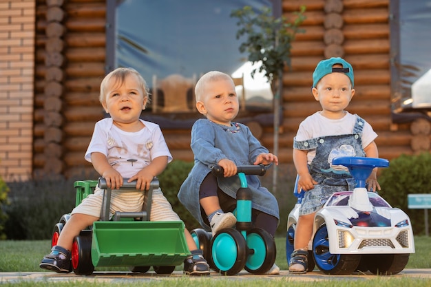 Three children ride on toy vehicles in the backyard