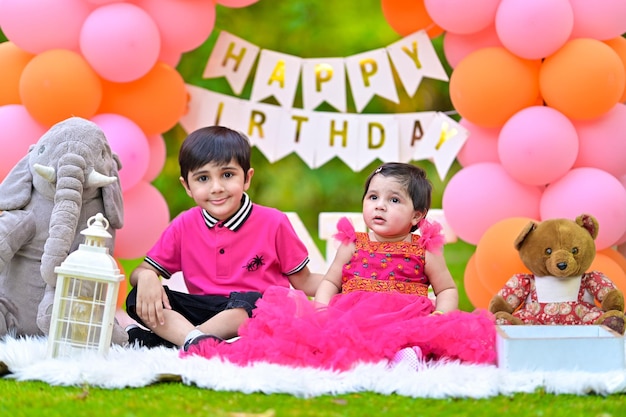 three children sitting on the grass with balloons and a banner that says happy birthday