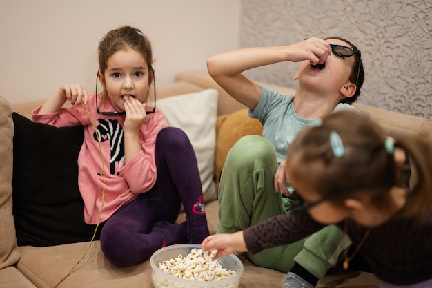 Three children sitting on the living room wear 3d glasses watching movie or cartoon