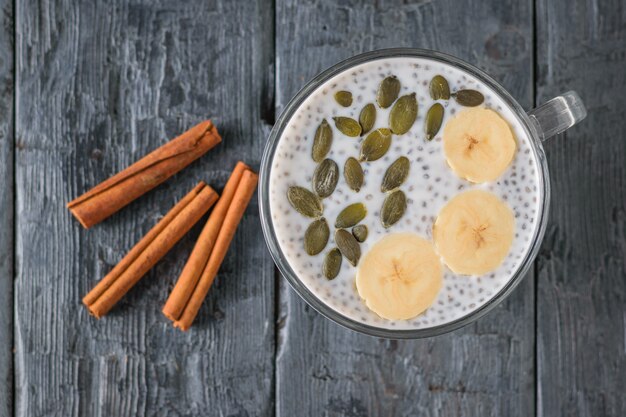 Three cinnamon sticks and a bowl of Chia seed pudding and bananas on a dark table. The view from the top. Flat lay.