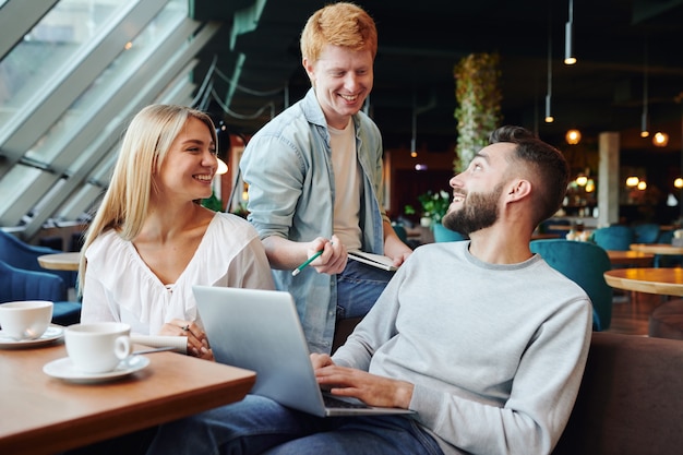 Three clever college students discussing points of project or presentation for conference while sitting in cafe after classes