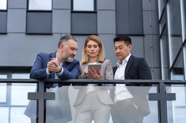 Three colleagues diverse business group business people outside office building talking and