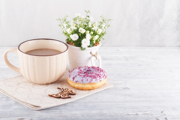 Three colorful donut, a cup of coffee and flowers on a white table