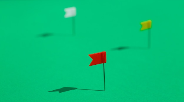 Three colorful little flag pins pinned on a green surface. Business or travel concept. The Goals .