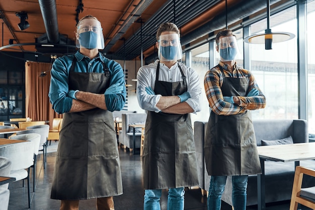 Photo three confident male waiters in protective workwear keeping arms crossed and