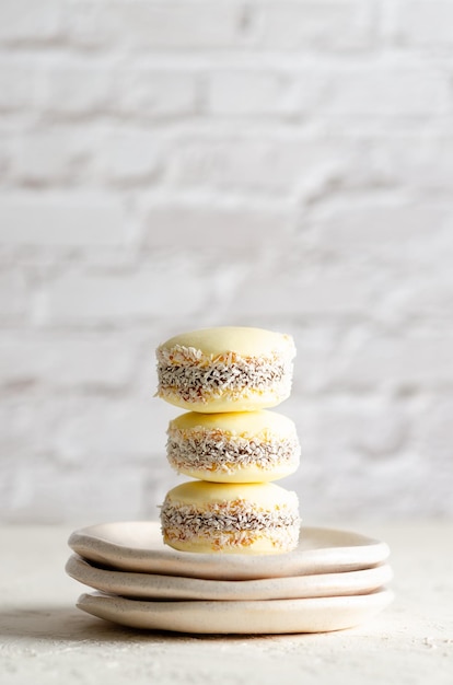 Three cornstarch alfajores with coconut on three little plates on white brick wall