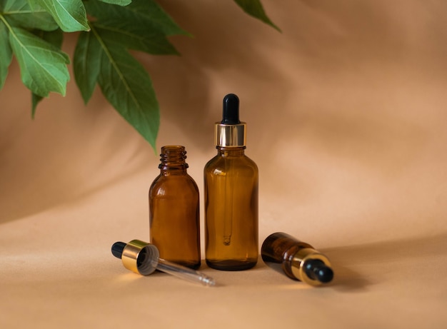 Three cosmetic bottles with a pipette on a beige background with leaves