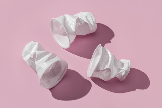 Three crumpled plastic, white cups on a pink background. Close-up, studio shot.