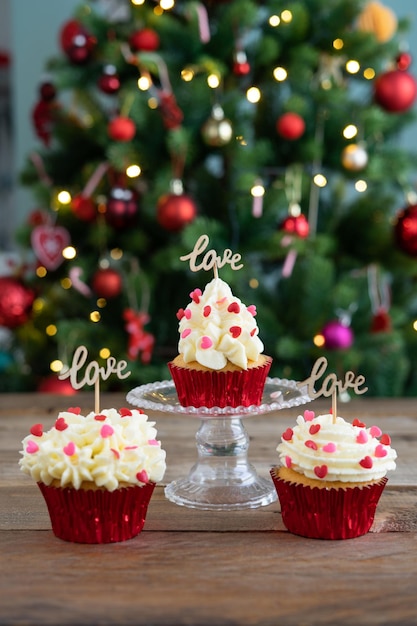 Three cupcakes decorated on wooden background with LOVE sign and Christmas tree Copy space Vertical photo