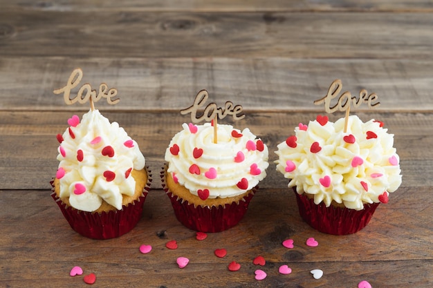 Three cupcakes with red topping decoration and a wooden sign with the word LOVE on a wooden background Copy space