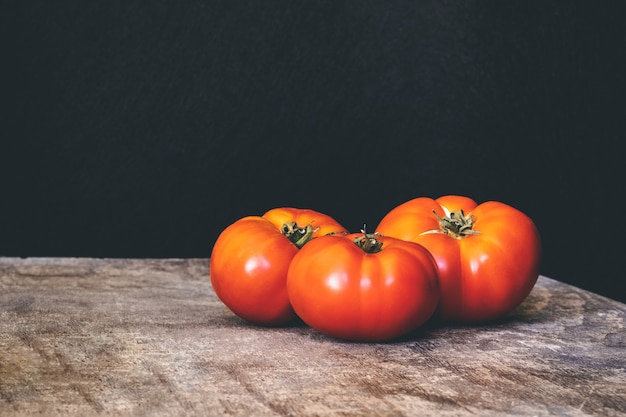 Three delicious fresh tomatoes on a rustic wooden table with black wall