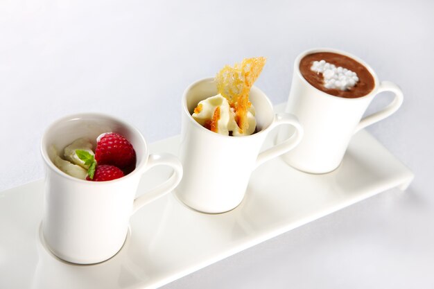 three different desserts in mugs over white background